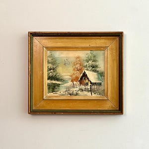 May include: A framed painting of a winter scene with a small cabin in the woods. The painting is in a gold frame and has a rustic feel.