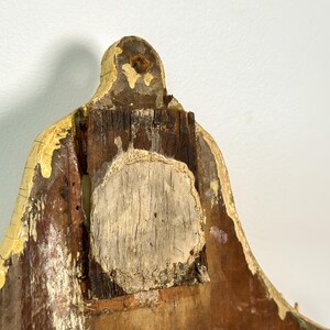 K&ouml;nnte beinhalten: Nahaufnahme eines verwitterten, h&ouml;lzernen Architekturelements mit einem verwitterten, gelb lackierten Rand. Das Holz weist Alters- und Abnutzungserscheinungen auf, mit freiliegender Maserung und einem zentralen, kreisf&ouml;rmigen Patch.