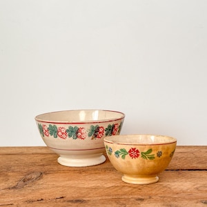 Peut inclure: Deux bols anciens en céramique avec des motifs floraux. Le plus grand a un bord rouge et un motif de fleurs rouges et vertes. Le plus petit a une teinte jaune avec des accents floraux rouges et bleus. Les deux bols sont sur une surface en bois.