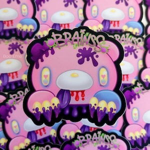 May include: A pink bear sticker with purple and yellow accents. The bear has a dripping purple substance and a red tongue. The sticker says "BRAINS" in purple letters.
