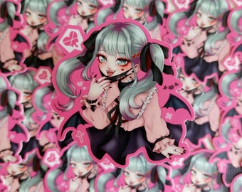 May include: A sticker featuring a cartoon illustration of a girl with green hair, wearing a pink dress, black wings, and a black mask with the word "Vampire" on it. She has a red heart with a cross through it on her cheek and is holding a finger to her lips. The sticker has a pink background with white hearts and a white cross.