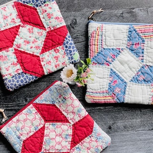 May include: Three square zippered pouches made from quilted fabric with patchwork designs. One pouch features red and floral patterns, another displays blue and white floral prints with striped accents, and the third shows red and light blue geometric motifs.