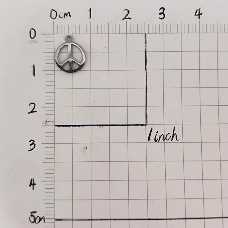 May include: A silver peace sign charm, measuring approximately 1 inch in diameter, is shown on a gridded surface.
