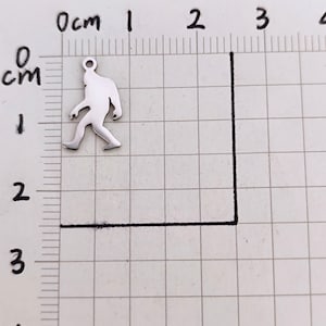 May include: A silver charm in the shape of a walking Bigfoot, approximately 2 cm tall.