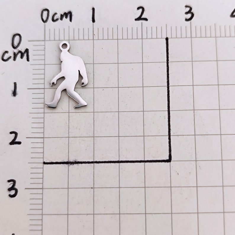 May include: A silver charm in the shape of a walking Bigfoot, approximately 2 cm tall.