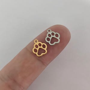 Peut inclure: Deux breloques en forme de patte de chien en métal, l'une dorée et l'autre argentée, sur un doigt.