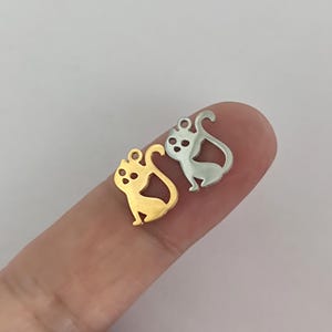 May include: Two metal cat charms, one gold and one silver, in the shape of a sitting cat. The charms are small and delicate, ideal for adding a touch of whimsy to jewellery or crafts.