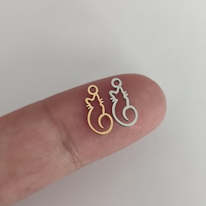 Op de afbeelding: Twee kleine katvormige bedels. De ene is goudkleurig, de andere zilverkleurig. Elke bedel heeft een lus aan de bovenkant om aan een ketting of armband te bevestigen. Het kattenontwerp is een eenvoudige omtrek met een gekrulde staart.