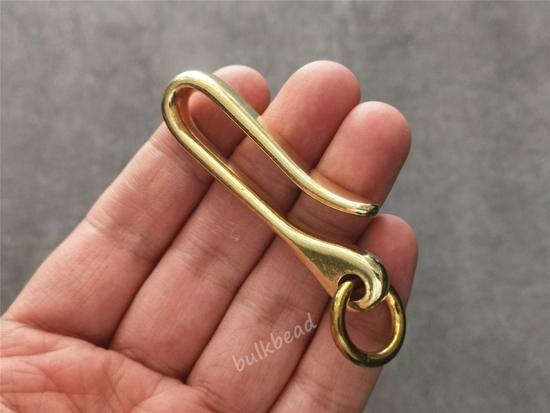 May include: A gold-colored metal key chain hook with a ring at the end. The hook is shaped like a letter 'S' and is designed to hold keys or other small items.