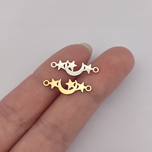 May include: Two metal charms in the shape of a crescent moon with three stars. The charm on the top is silver and the charm on the bottom is gold.