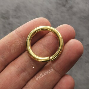 Puede incluir: Un anillo de salto de metal de color dorado se sostiene en una mano. El anillo es liso y tiene una forma circular.