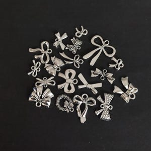 Könnte beinhalten: Eine Sammlung von silberfarbenen Metall-Schleifenanhängern. Die Anhänger sind in verschiedenen Größen und Stilen, einige mit einer einfachen Schleifenform und andere mit aufwendigeren Details.