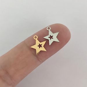 Può includere: Due ciondoli a forma di stella, uno dorato e uno argentato, con una piccola stella ritagliata al centro di ciascuno. I ciondoli hanno un anello nella parte superiore per essere attaccati a gioielli o altri oggetti artigianali.