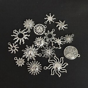 Pode incluir: Uma coleção de pingentes de sol de metal prateado com vários designs, incluindo rostos, raios e círculos simples. Os pingentes têm argolas de salto para serem presos a joias ou outros artesanatos.