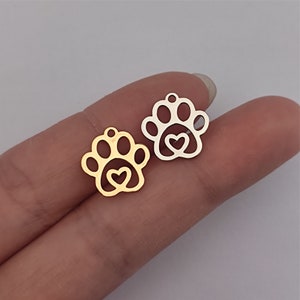 May include: Two metal charms in the shape of a paw print with a heart inside. One charm is gold and the other is silver.
