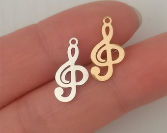 May include: Two metal treble clef charms, one gold and one silver, on a finger.