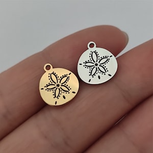 May include: Two metal charms in the shape of a sand dollar with a black flower design. One charm is gold and the other is silver.