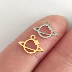 Peut inclure: Deux petits breloques en forme de planète. L'une est dorée, l'autre argentée. Chaque breloque représente une planète avec un anneau et une étoile. Les breloques sont en métal et ont une petite boucle en haut pour la bijouterie.