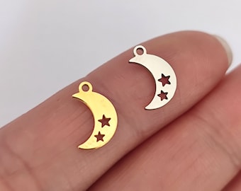 May include: Two metal charms in the shape of a crescent moon with three stars cut out. One charm is gold and the other is silver.