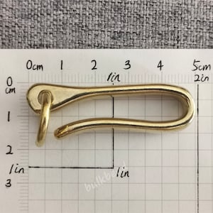 May include: A gold-colored metal hook with a rounded opening. The hook is about 5 cm long and is measured against a ruler.