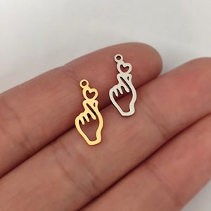 May include: Two metal charms in the shape of a hand making a heart sign with a small heart on the fingertip. One charm is gold and the other is silver.