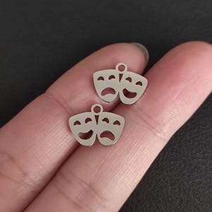 May include: Two silver charm pendants shaped like theatre masks. One mask is smiling and the other is frowning.