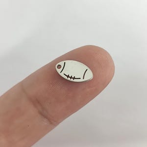 May include: Silver charm shaped like a football with a hole at the top for attaching to a necklace or bracelet.