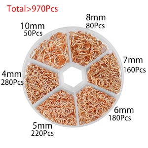 May include: A white plastic container with six compartments filled with gold jump rings in various sizes. The container is labeled with the size and quantity of each ring type: 4mm (280Pcs), 5mm (220Pcs), 6mm (180Pcs), 7mm (160Pcs), 8mm (80Pcs), and 10mm (50Pcs). The total number of jump rings is 970.