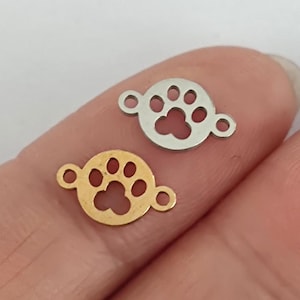 May include: Two metal paw print charms, one gold and one silver, with a circular shape and a hole on each side for attaching to jewellery.