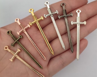 May include: Six sword charms in different metal finishes: gold, rose gold, silver, bronze, and gunmetal. The swords have a detailed design with a cross guard and a pointed tip.