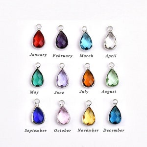 May include: Twelve teardrop-shaped crystal charms in various colors, representing each month of the year. January is red, February is purple, March is blue, April is clear, May is green, June is lavender, July is orange, August is light green, September is blue, October is pink, November is yellow, and December is dark blue.