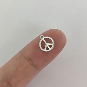May include: Silver peace sign charm pendant. The charm is a circle with a peace sign inside. The charm is small and would be perfect for adding to a necklace or bracelet.