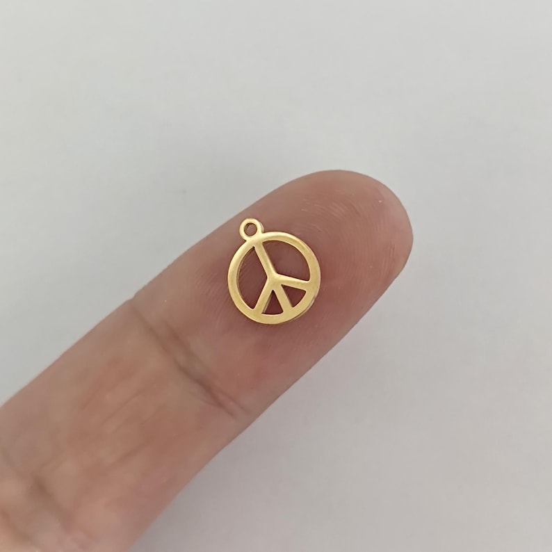 May include: Gold peace sign charm pendant. The charm is a simple, circular design with a peace sign inside.