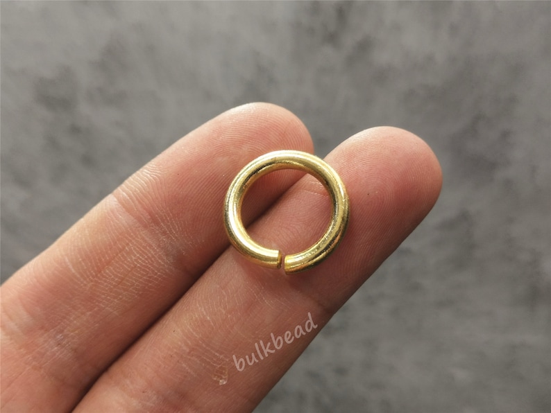 Puede incluir: Un anillo de salto de metal de color dorado. El anillo es redondo y tiene un acabado liso.