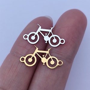 Könnte beinhalten: Zwei Fahrrad-Anhänger aus Metall, einer golden und einer silbern, mit einem schlichten Design. Die Anhänger eignen sich perfekt, um Schmuck oder Bastelarbeiten eine persönliche Note zu verleihen.