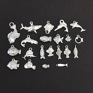 May include: A collection of 20 silver-toned metal fish charms, including a shark, a stingray, a dolphin, and various types of fish. The charms are perfect for jewelry making, scrapbooking, and other craft projects.
