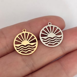 Könnte beinhalten: Zwei Metall-Anhänger in Form einer Sonne, die über dem Meer untergeht. Ein Anhänger ist golden und der andere ist silber.