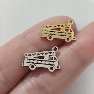 May include: Two metal fire truck charms, one gold and one silver. The charms are detailed with a ladder and windows. They are perfect for adding a touch of whimsy to jewelry or crafts.