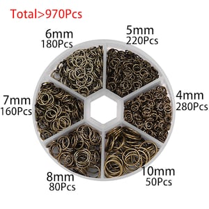 May include: A white plastic container with six compartments filled with different sizes of bronze jump rings. The container is labeled with the total number of jump rings, "Total>970Pcs", and the size and quantity of each size of jump ring.