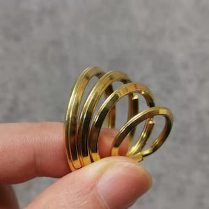 Può includere: Un set di quattro portachiavi in metallo color oro, impilati in ordine di grandezza graduata, con il portachiavi più grande in basso e il più piccolo in alto.