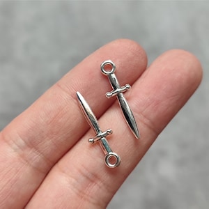 May include: Two silver-toned sword charms with a loop at the top for attaching to jewelry or other crafts.