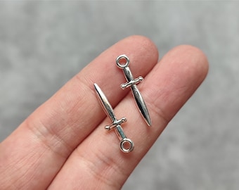 Könnte beinhalten: Zwei silberfarbene Schwertschmuckstücke mit einer Öse oben zum Anbringen an Schmuck oder anderen Bastelarbeiten.