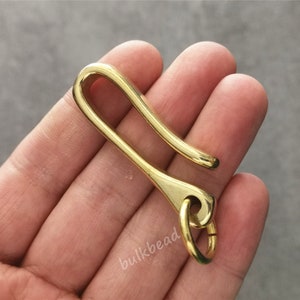 May include: A gold-colored metal key chain hook with a rounded loop at the end. The hook is designed to hold keys or other small items.