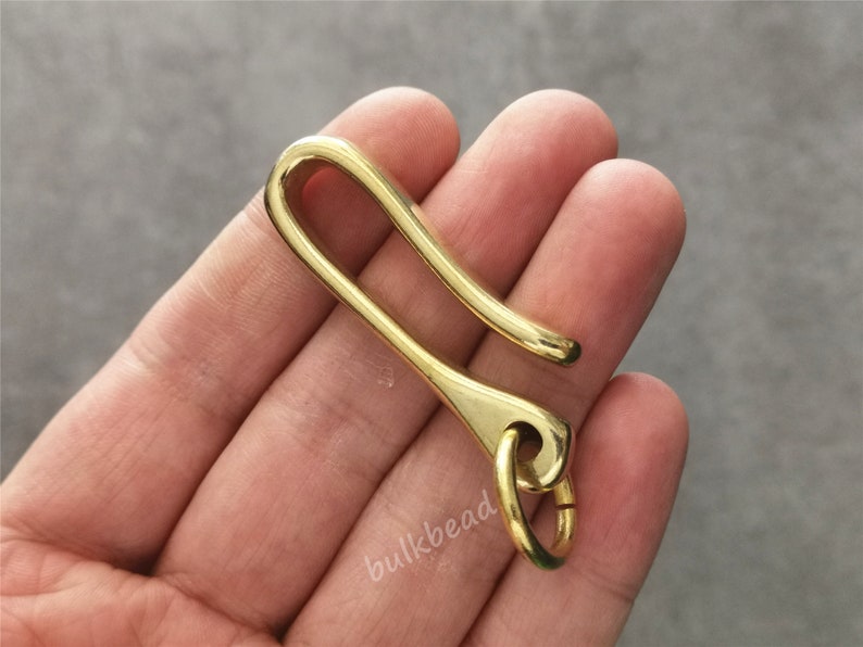 May include: A gold-colored metal key chain hook with a rounded loop at the end. The hook is designed to hold keys or other small items.