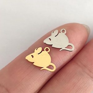 Könnte beinhalten: Zwei Metall-Maus-Anhänger, einer golden und einer silbern, auf einem Finger. Die Anhänger sind einfache Silhouetten von Mäusen.