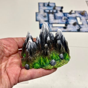 May include: A miniature mountain range with snow-capped peaks and green foliage, perfect for tabletop gaming or miniature scenery.