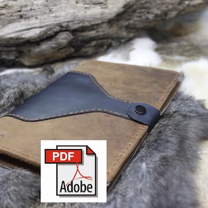 May include: A brown leather notebook with a black leather flap and a snap closure. The notebook is lying on a faux fur surface. The text "PDF Adobe" is visible on a white label.