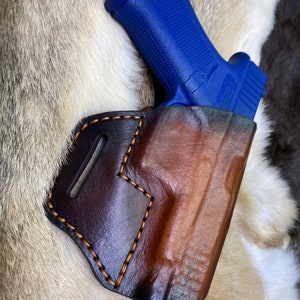 Può includere: Un fodero in pelle marrone con un bordo cucito e una pistola blu all'interno.