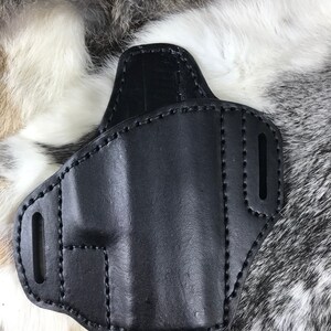 Könnte beinhalten: Schwarzes Lederholster mit Nähten. Das Holster hat zwei Ausschnitte an der Seite.