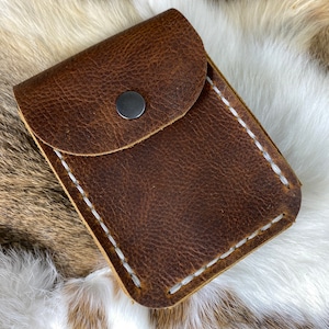 May include: A brown leather wallet with a flap closure and a white stitch detail. The wallet has a single snap closure.